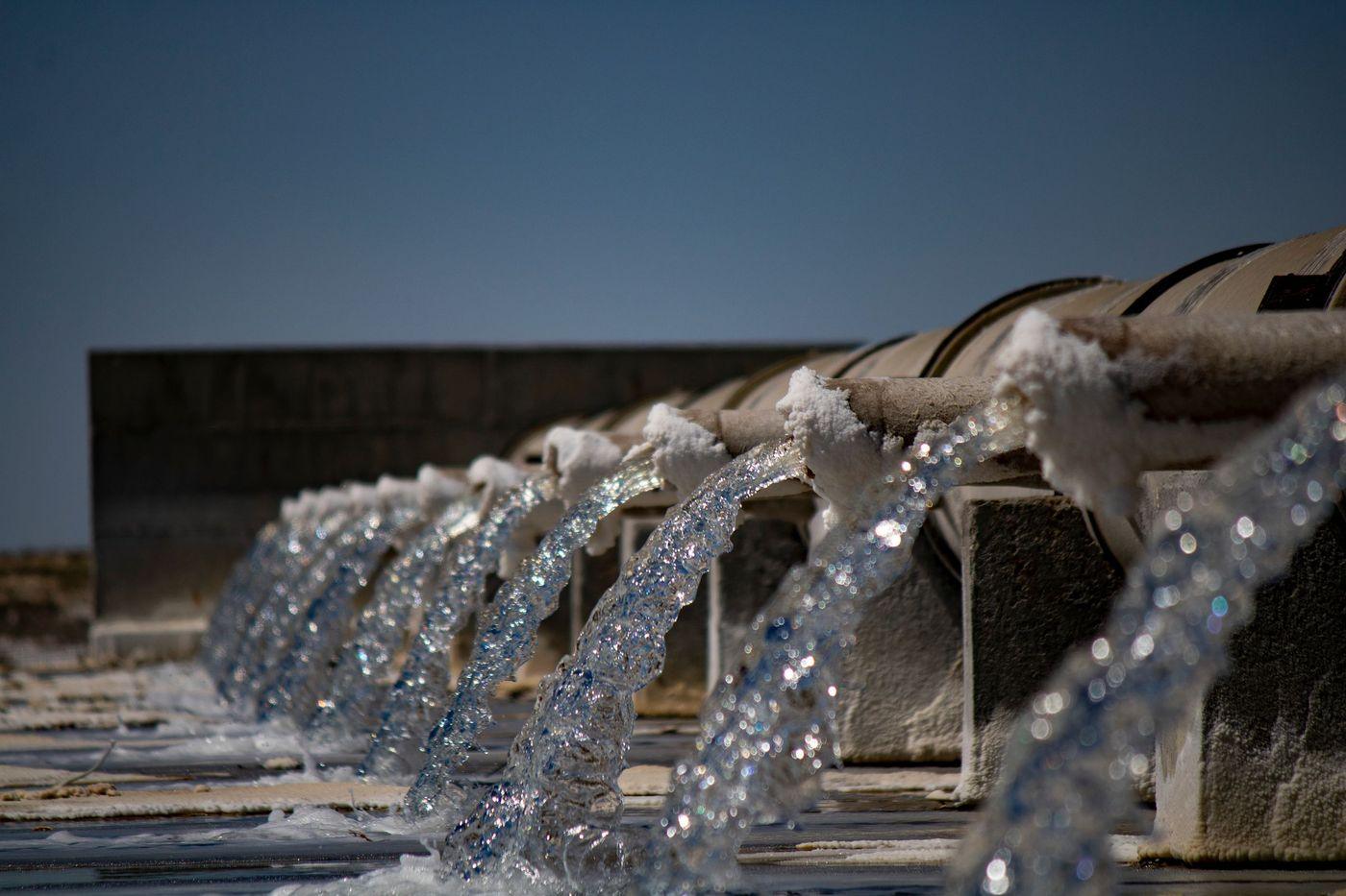 Water flowing from large industrial pipes at a coastal treatment facility under a clear sky